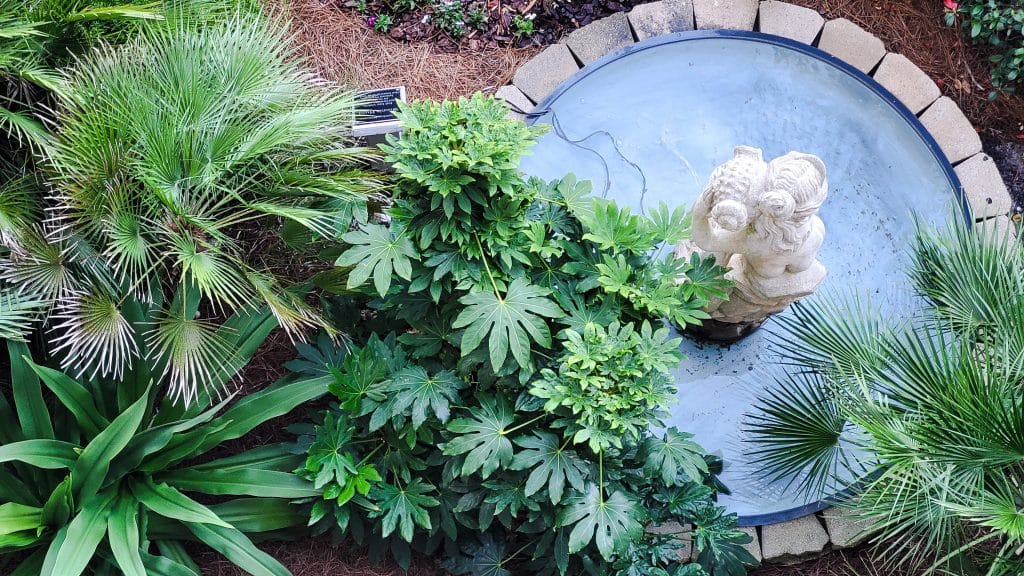 A decorative feature outside a condo has plants and a fountain with a water feature.